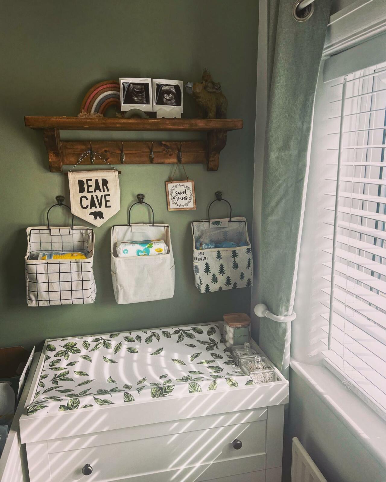 A sage green nursery with a changing table and shelves.