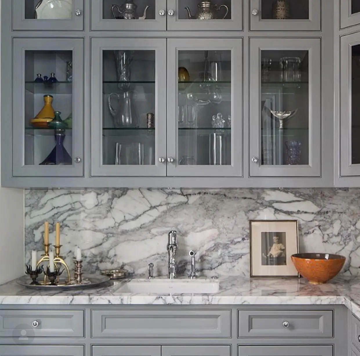 A kitchen with gray cabinets and marble counter tops.