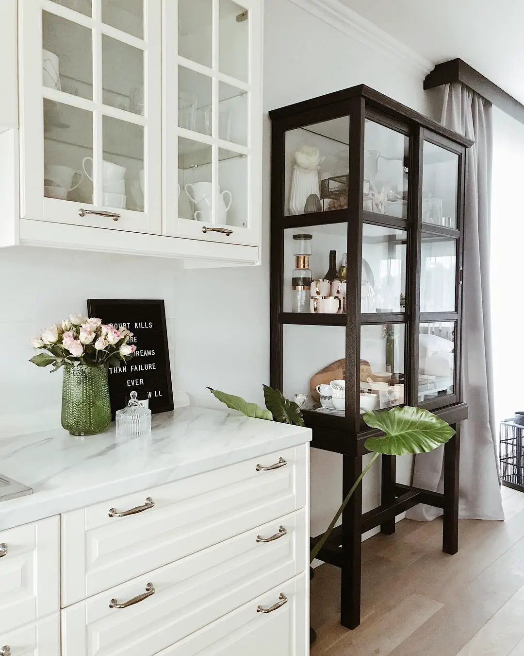A white kitchen with a glass cabinet and marble counter top.