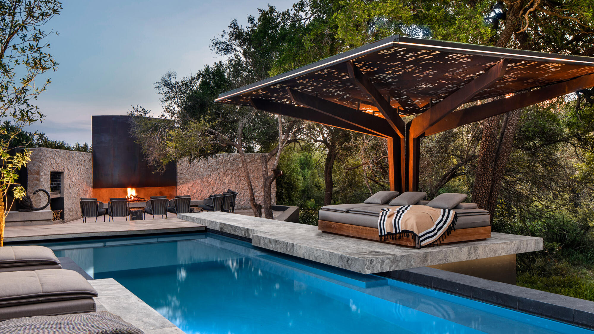A swimming pool with lounge chairs and a fire pit at Cheetah Plains: A Modernist Marvel.