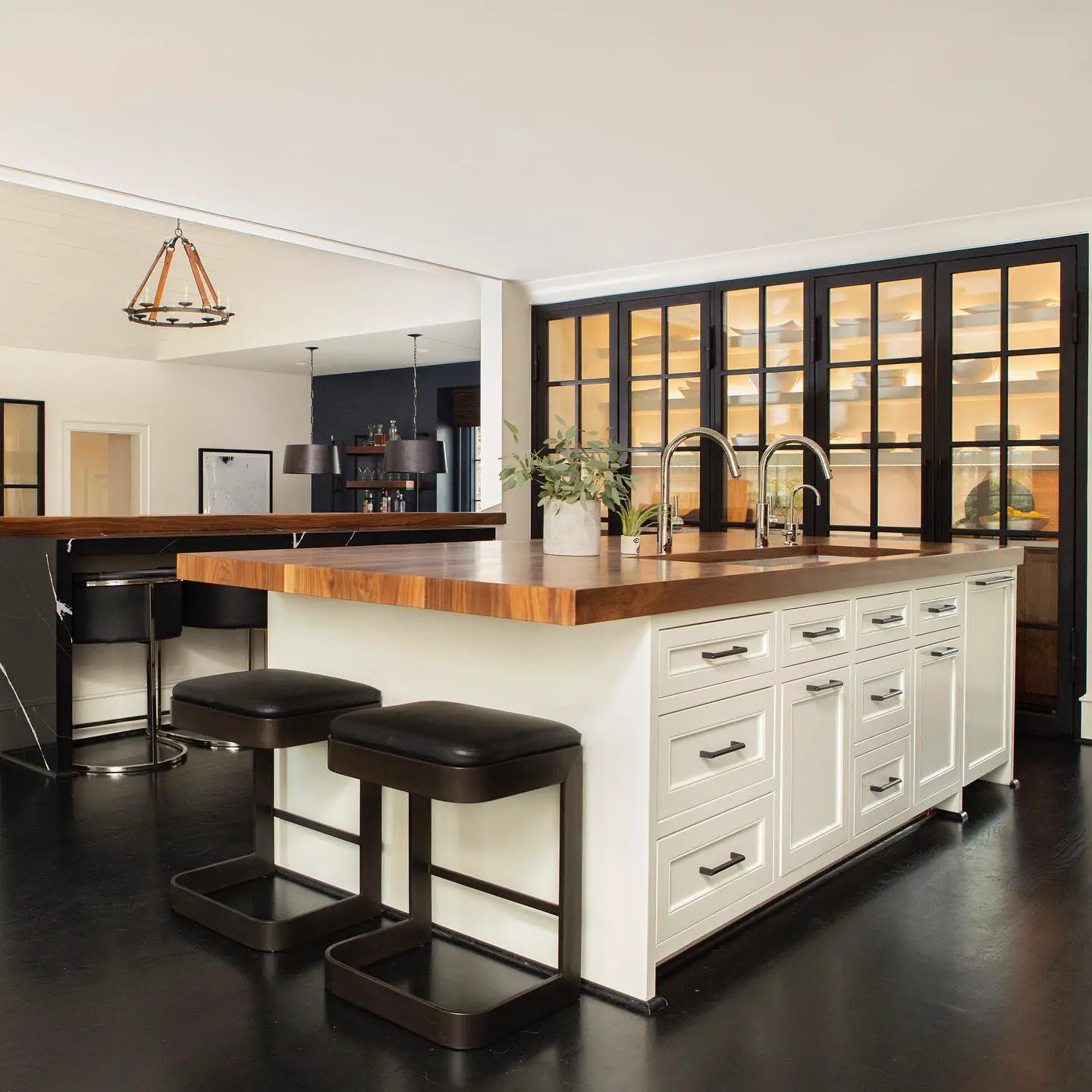 A kitchen with a large island and stools featuring a black kitchen floor.