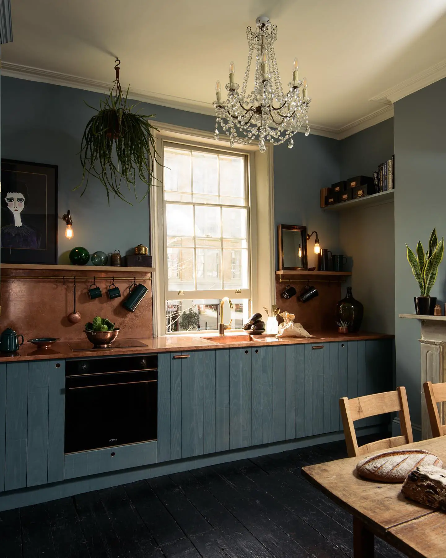 A blue kitchen with a black kitchen floor and wooden table and chairs.