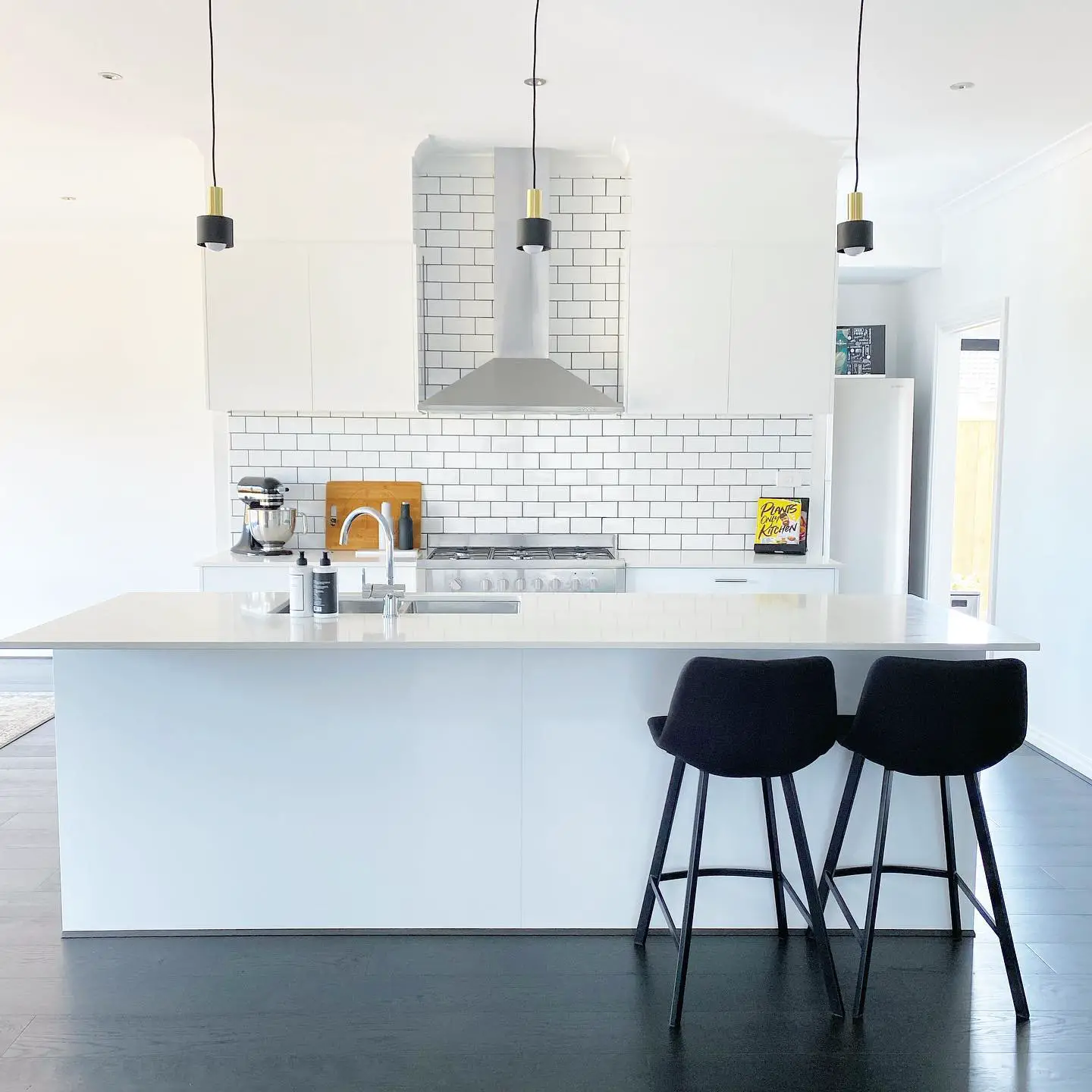 A white kitchen with black counter tops and stools, featuring a black kitchen floor.