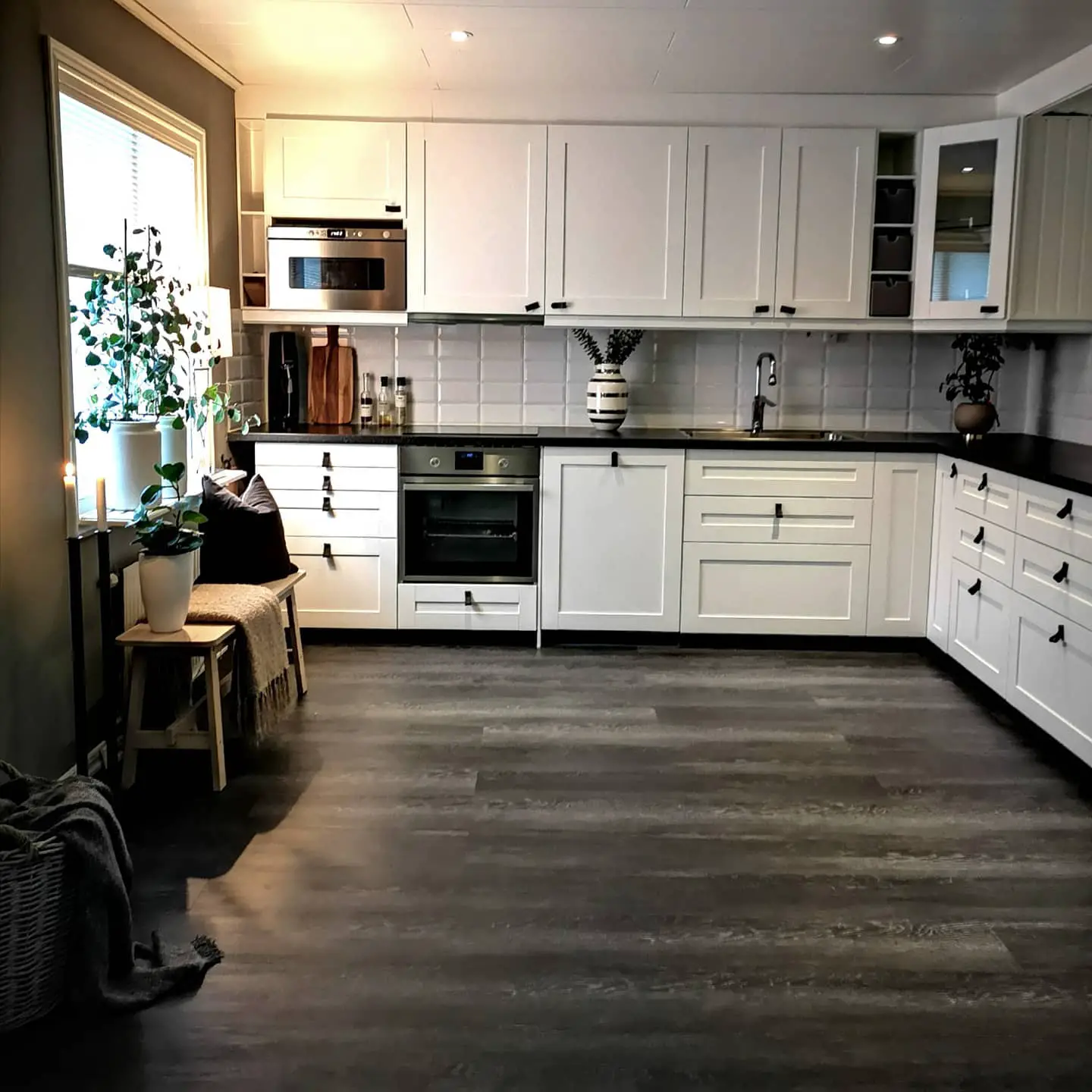 A kitchen with white cabinets and wood floors featuring a black kitchen floor.