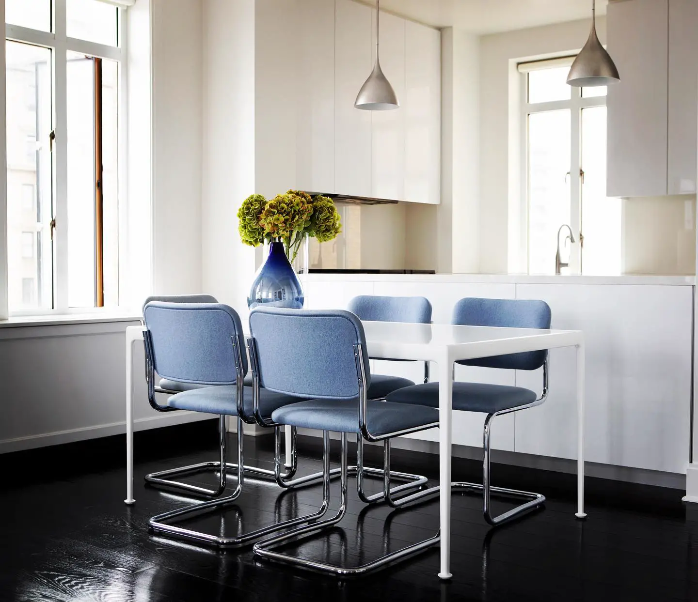 A white kitchen with blue chairs and a black kitchen floor.