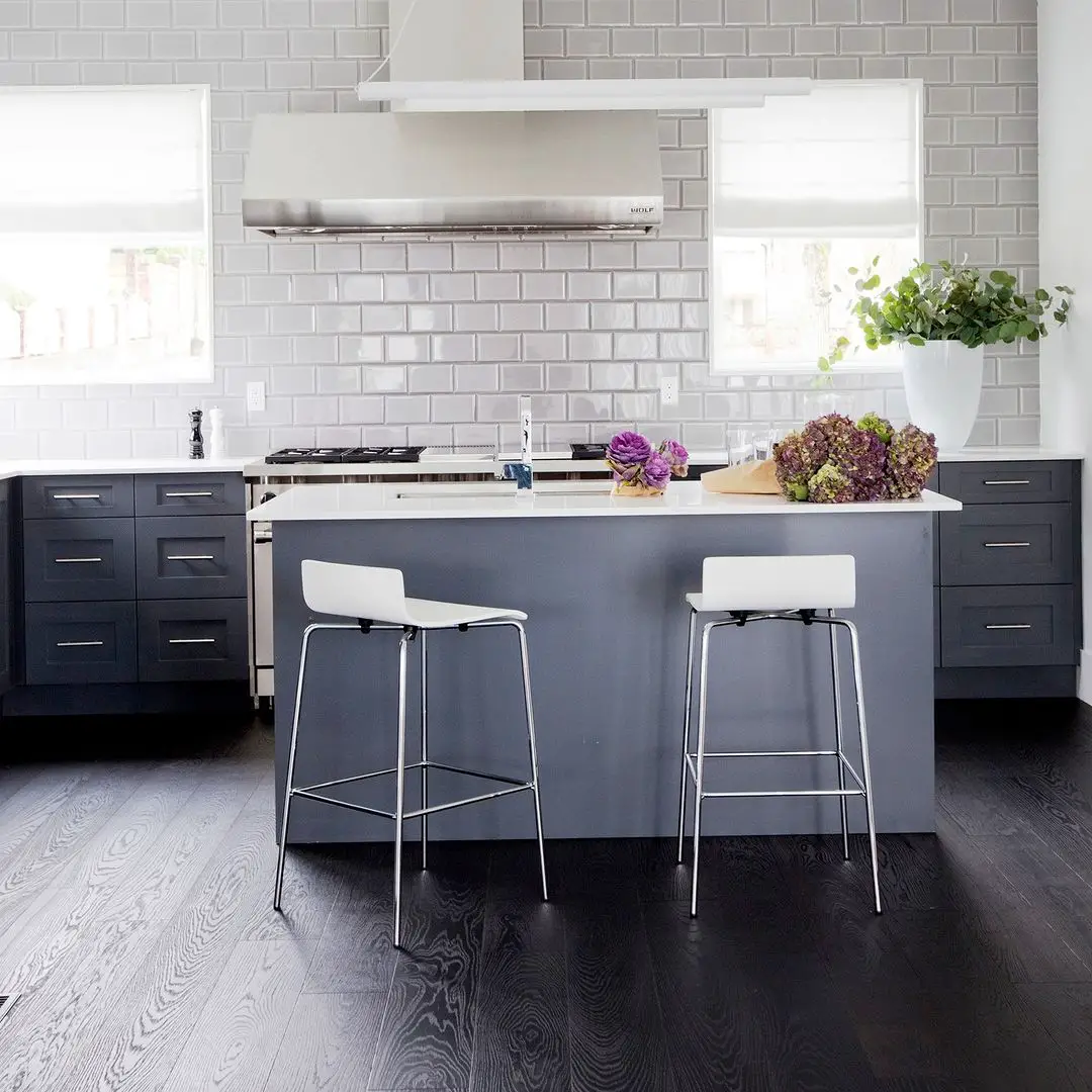 A kitchen with a gray island and black stools on a black kitchen floor.