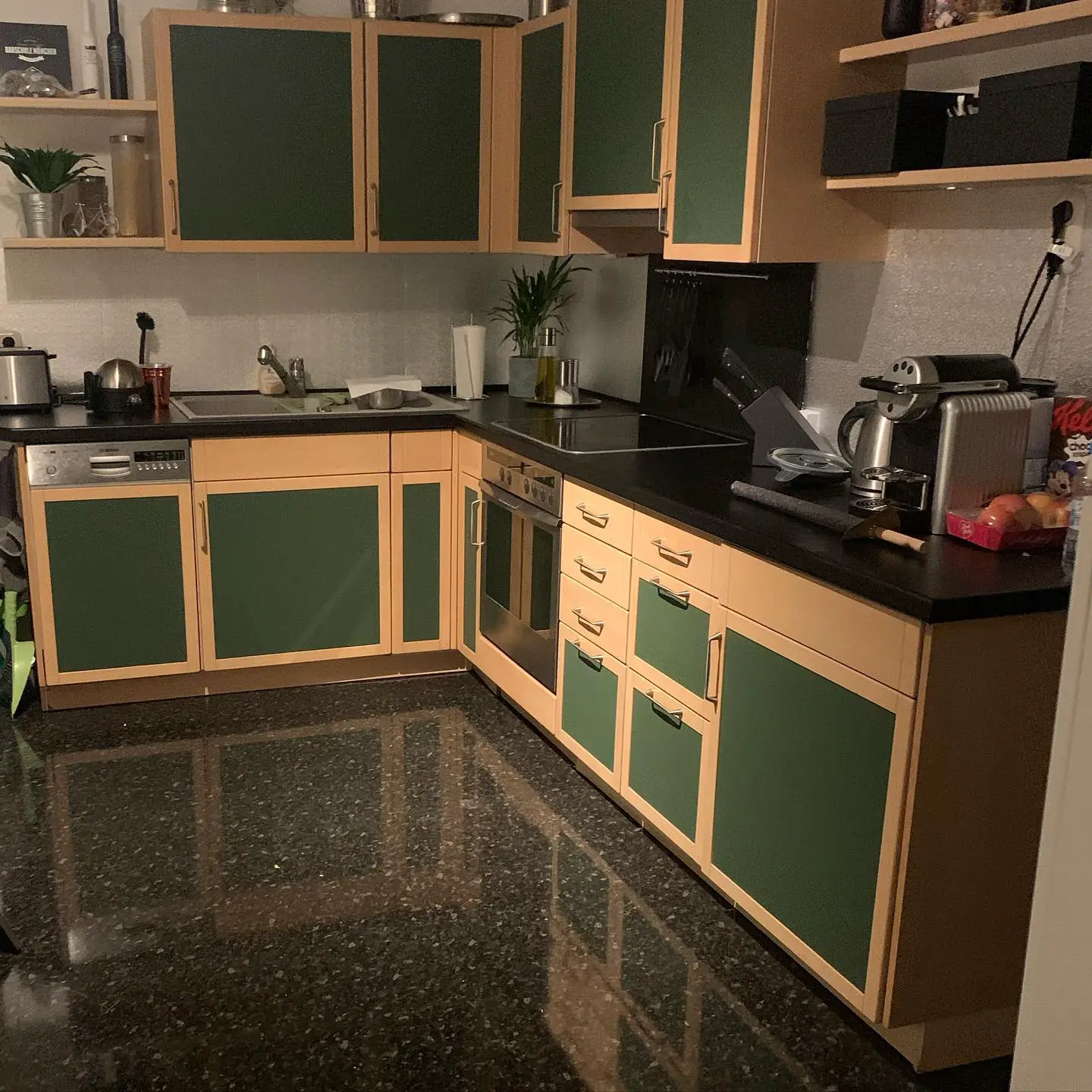 A kitchen with black countertops and green cabinets.