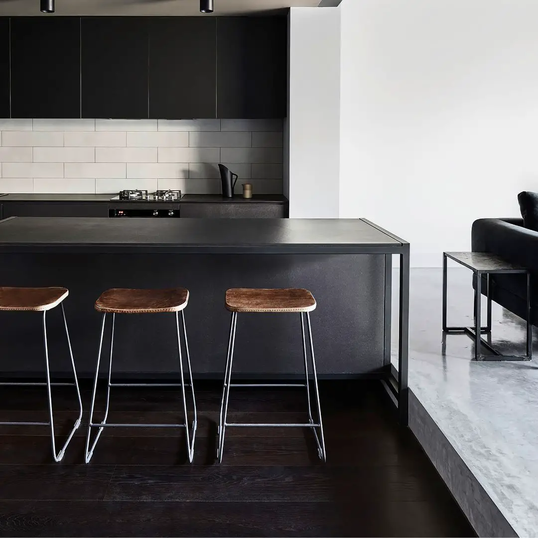 A modern kitchen with black cabinets and stools, featuring a black floor.