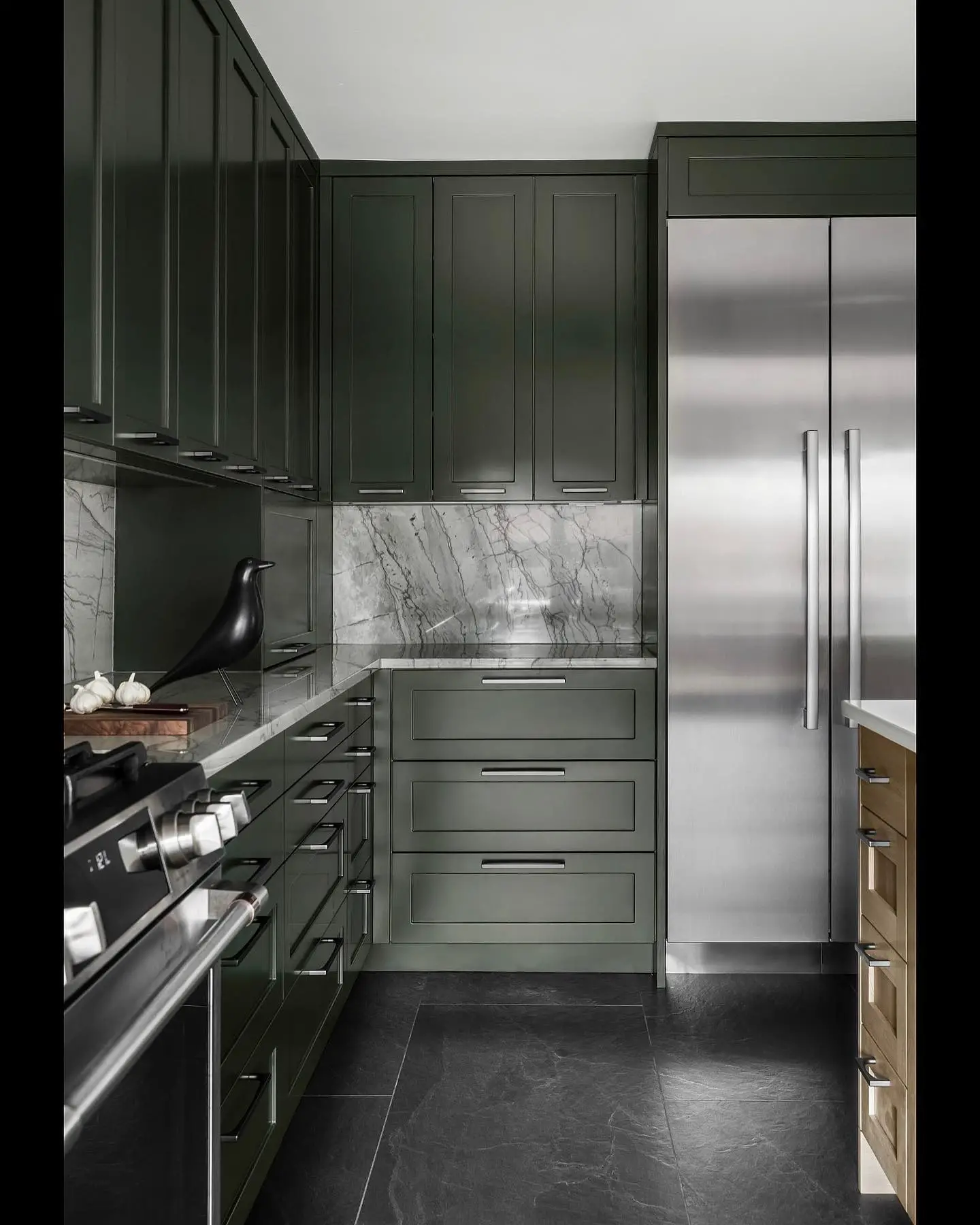 A kitchen with green cabinets and stainless steel appliances has a black kitchen floor.