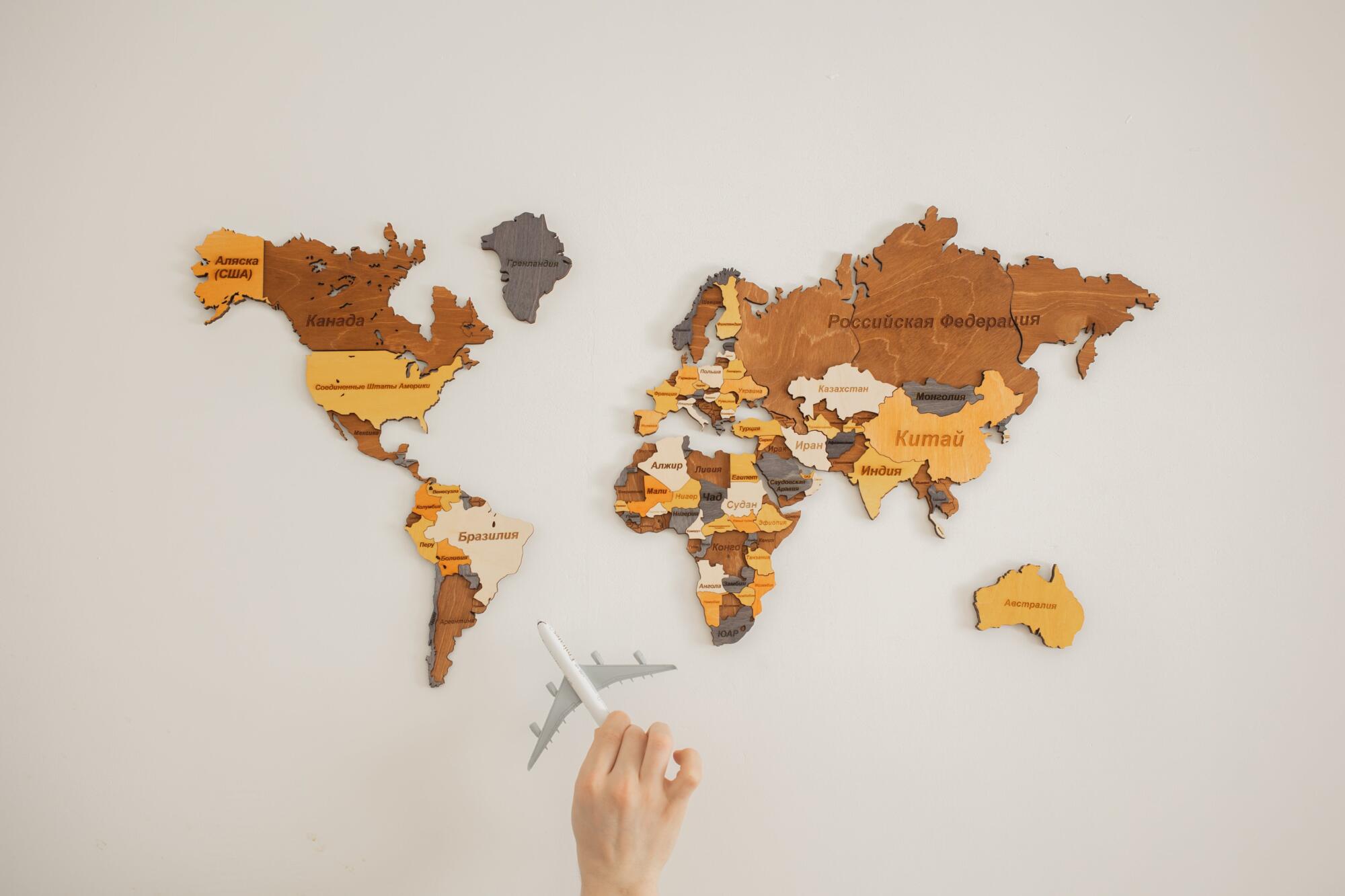 A person is holding a wooden world map, showcasing cultural fusion, in front of a white wall.