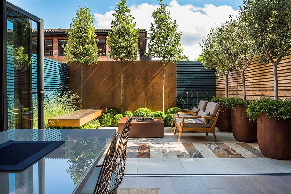 Modern backyard garden with seating and olive trees.