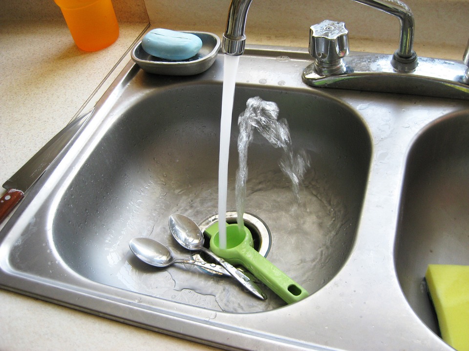 Running water over utensils in kitchen sink.