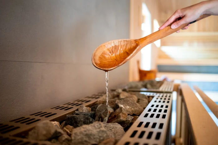 Pouring water on sauna rocks with wooden ladle.