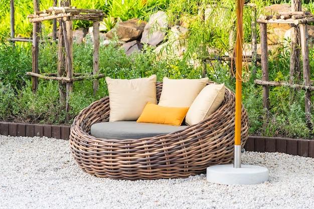 Outdoor wicker sofa with cushions and garden background.