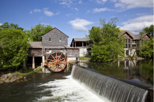 Historic watermill with large wheel by waterfall.