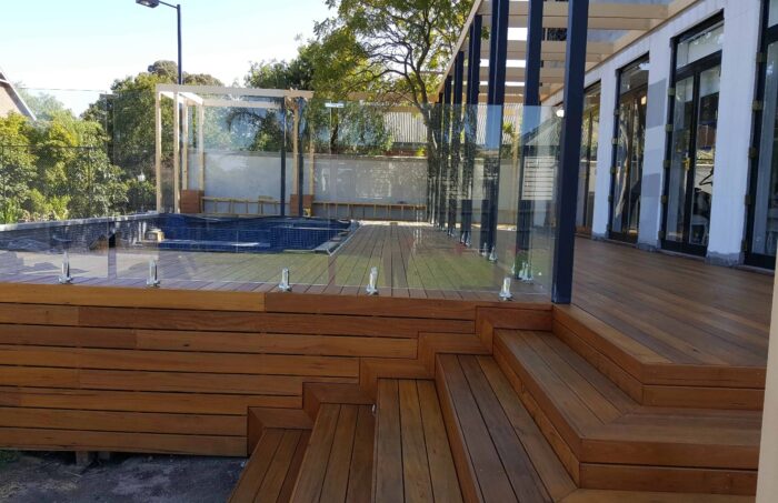 Modern wooden deck with glass railing and pool
