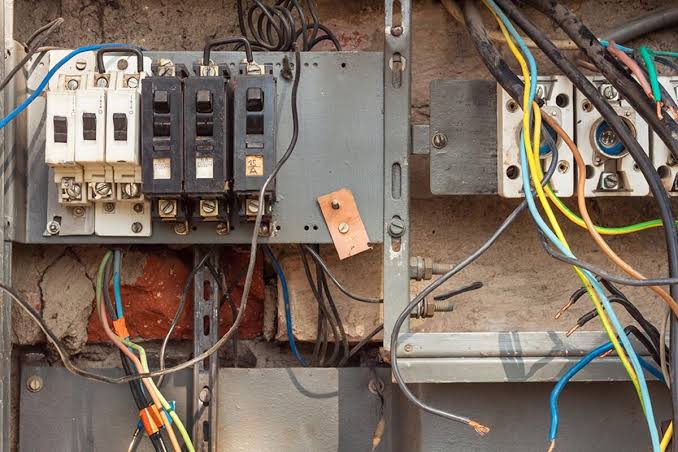 Exposed electrical panel with tangled wires and circuit breakers