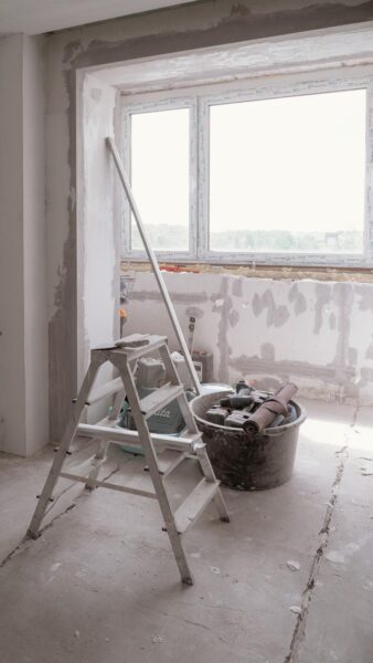 Unfinished home renovation with tools, ladder, exposed drywall, and large window