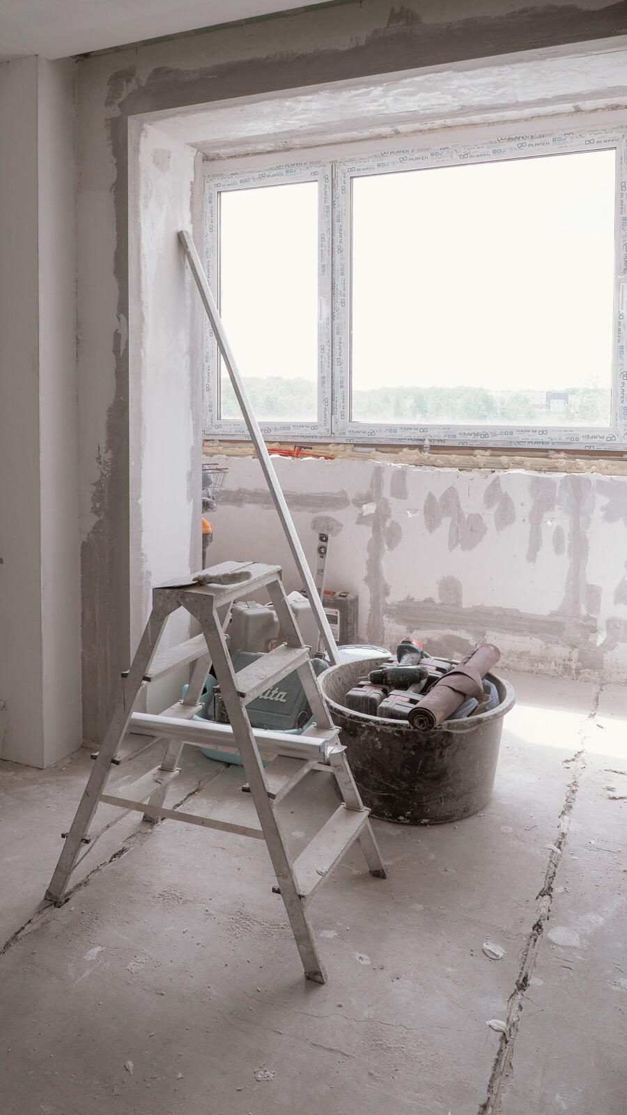 Unfinished home renovation with tools, ladder, exposed drywall, and large window
