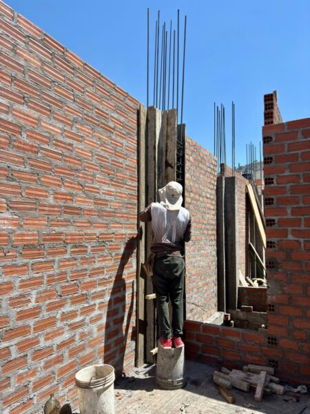 Worker constructing brick walls with reinforced concrete columns and vertical steel rebar