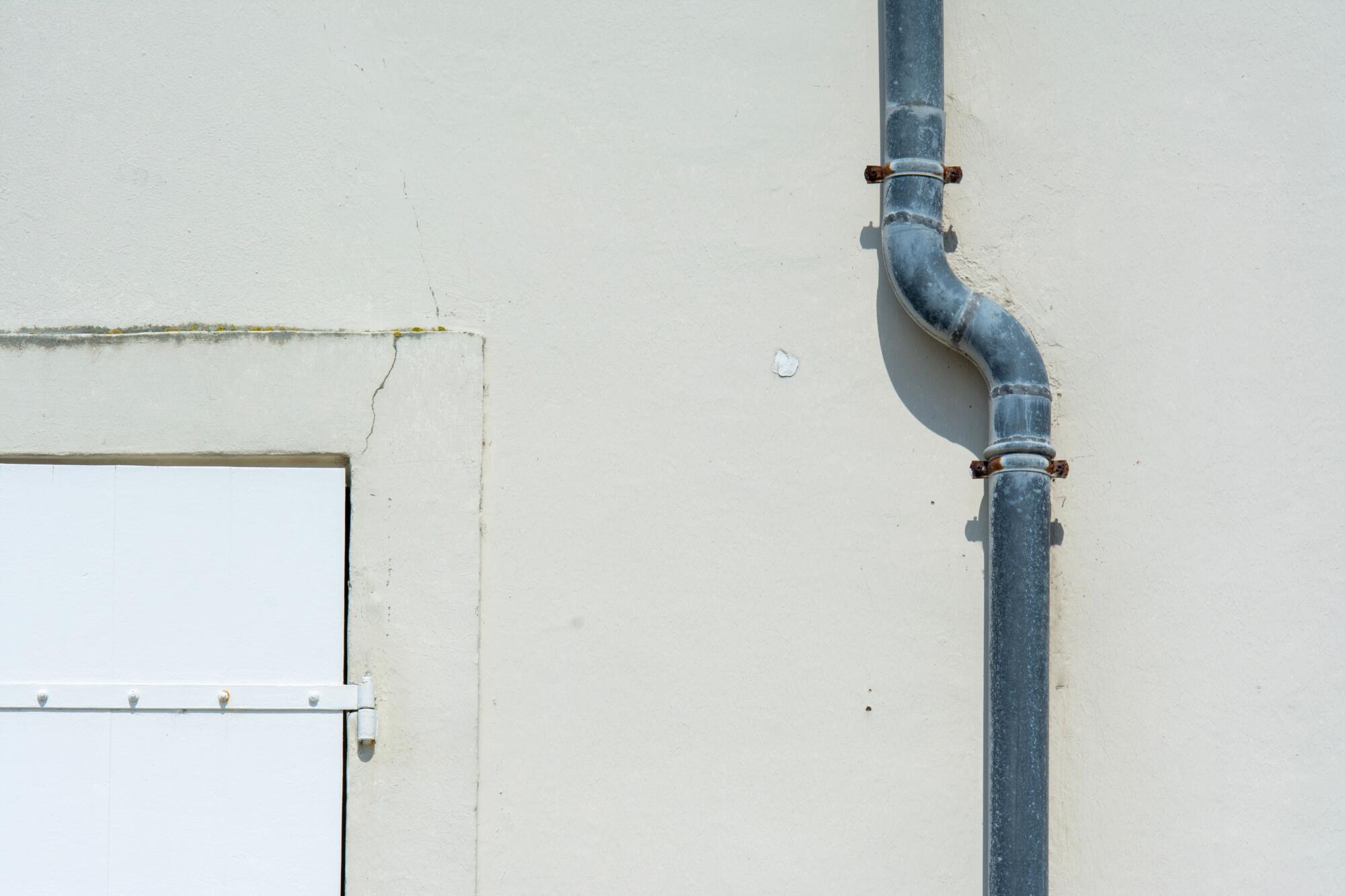 Curved metal drainpipe on a cracked white exterior wall