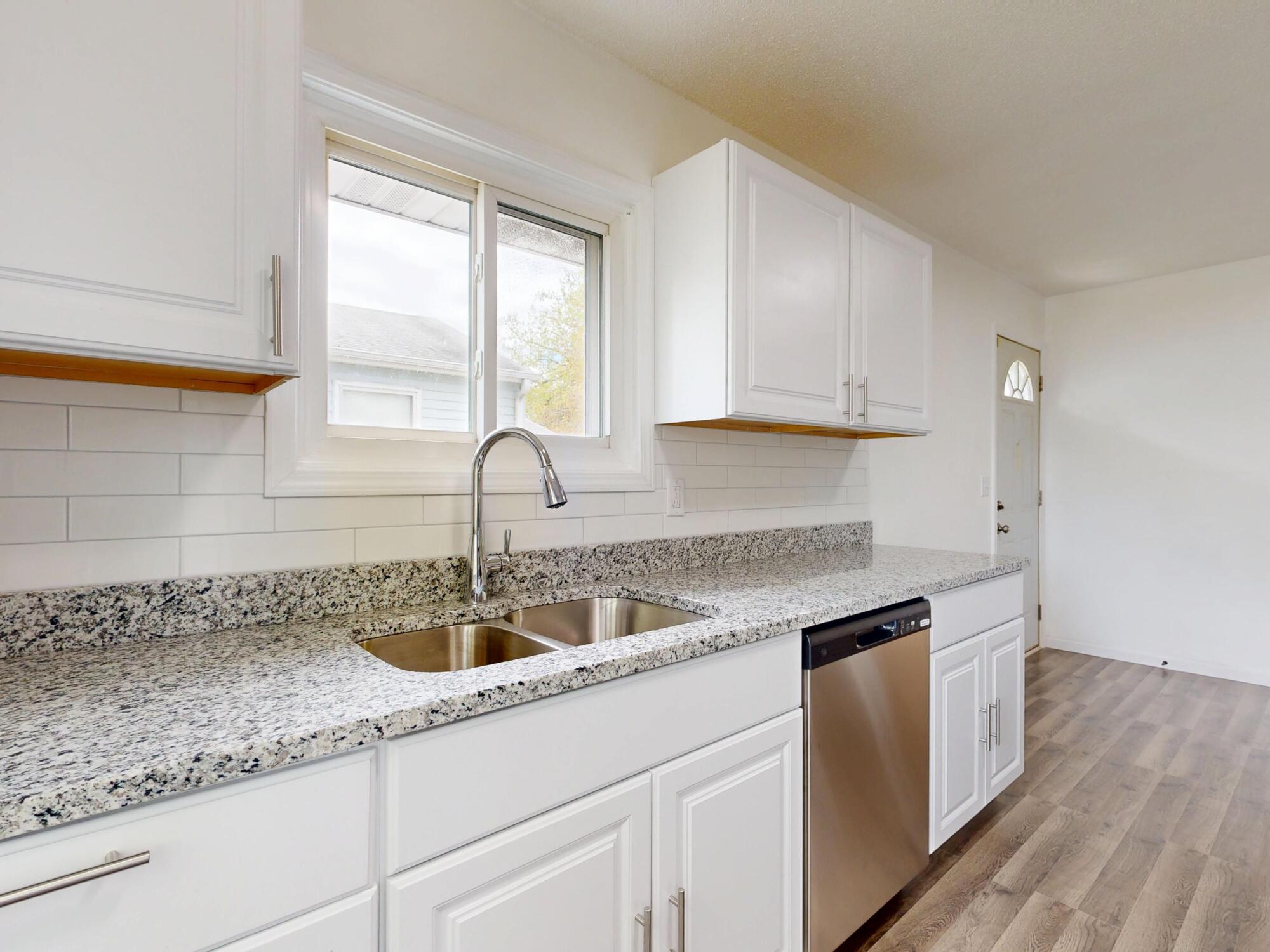 Bright white kitchen with painted cabinets, granite countertops, subway tile backsplash, and stainless steel dishwasher