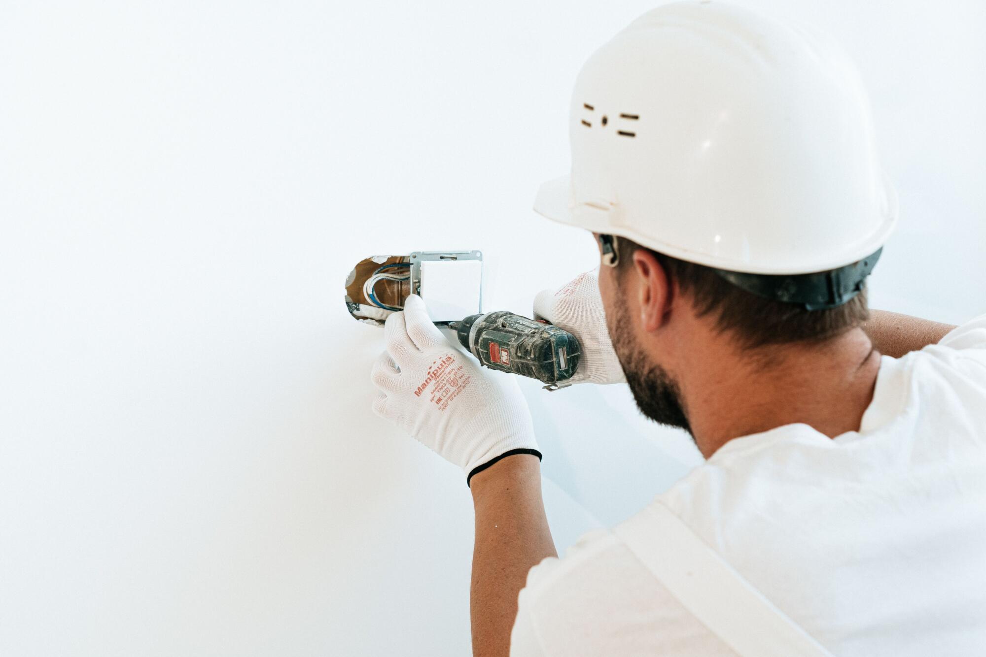 Electrician installs wall switch using cordless drill