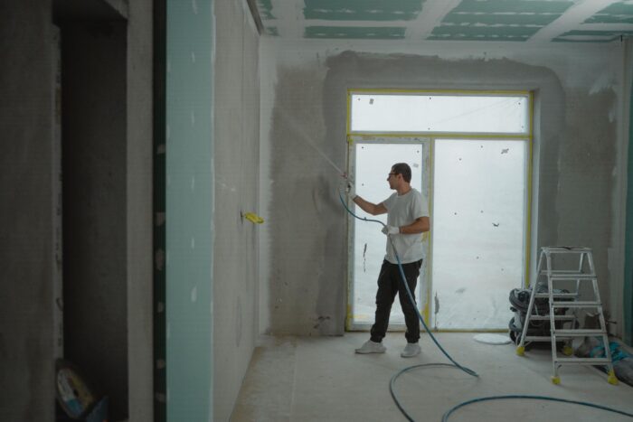 Contractor applying a spray coating to an unfinished wall during a home renovation project.