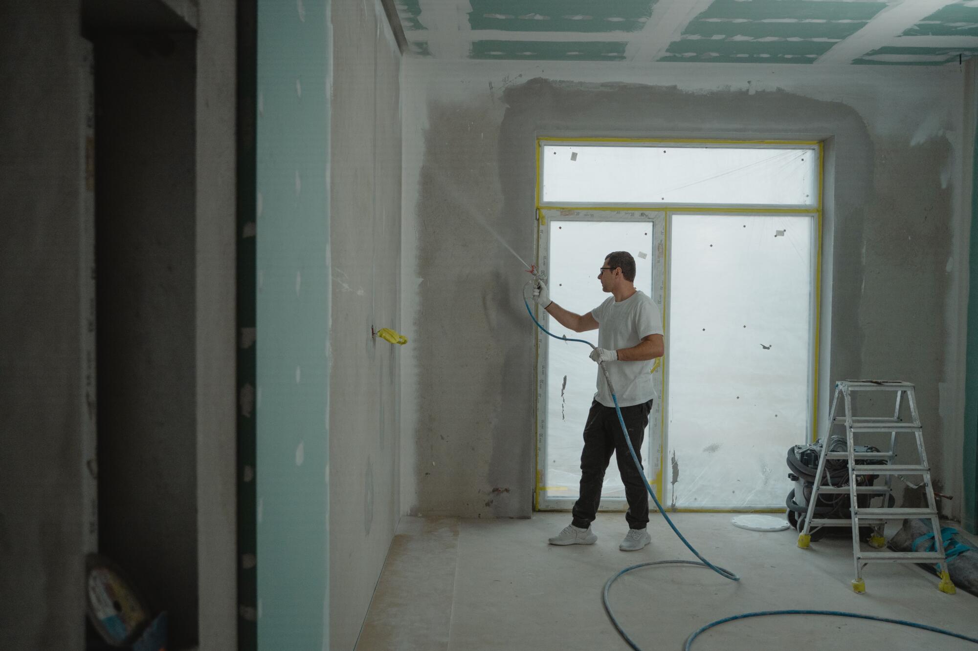 Contractor applying a spray coating to an unfinished wall during a home renovation project.